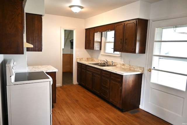 kitchen featuring dark brown cabinetry, range, wood finished floors, a sink, and light countertops