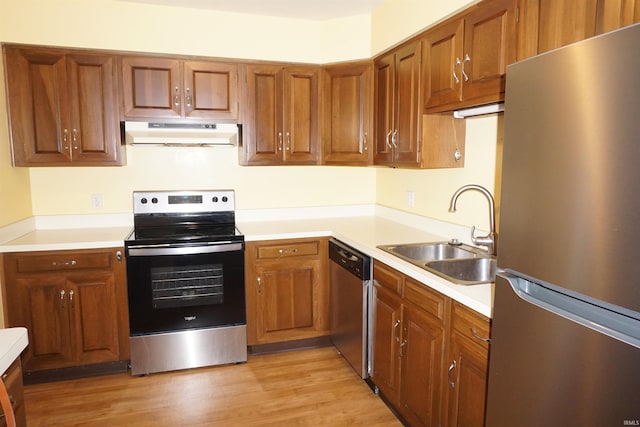 kitchen with brown cabinets, appliances with stainless steel finishes, a sink, light countertops, and under cabinet range hood
