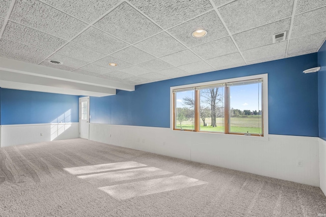 carpeted spare room featuring visible vents, plenty of natural light, a paneled ceiling, and a wainscoted wall