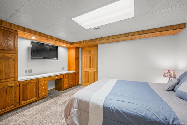 bedroom with visible vents, built in study area, a drop ceiling, and light carpet