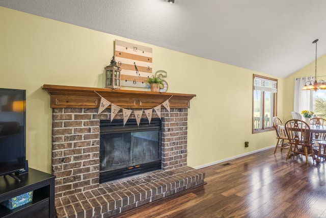 living area featuring a fireplace, vaulted ceiling, wood finished floors, baseboards, and an inviting chandelier