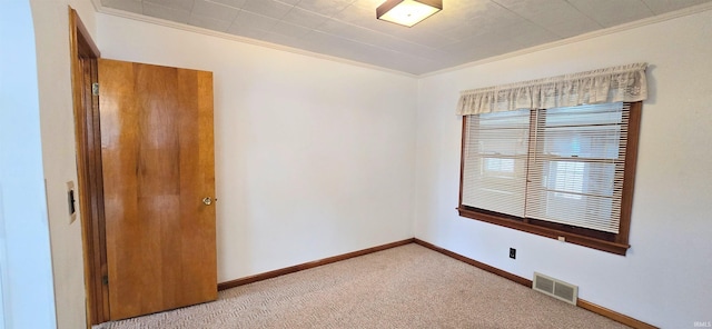 empty room featuring light colored carpet, baseboards, visible vents, and ornamental molding