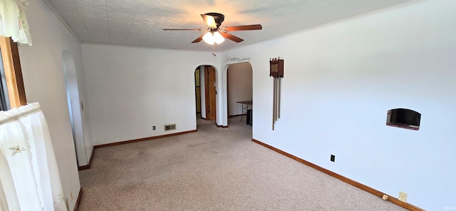 carpeted empty room with visible vents, arched walkways, ceiling fan, and ornamental molding