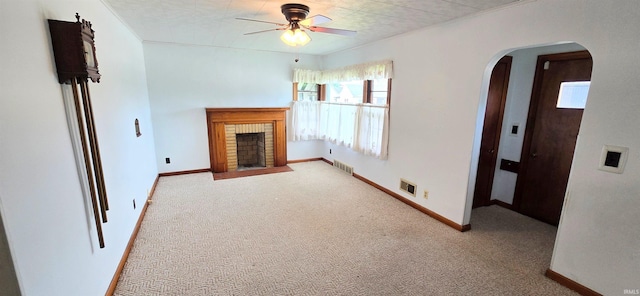 unfurnished living room featuring plenty of natural light, a ceiling fan, visible vents, arched walkways, and carpet floors