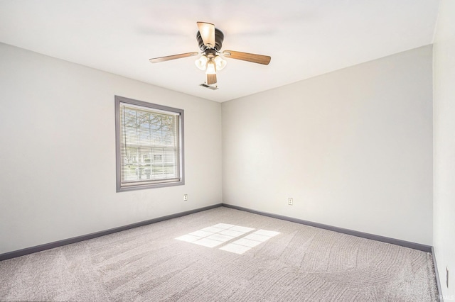 spare room featuring light colored carpet, a ceiling fan, and baseboards