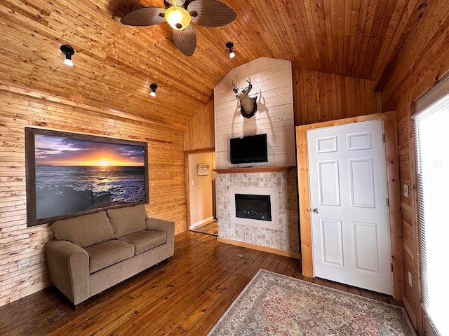 living area with wood walls, hardwood / wood-style floors, ceiling fan, a tile fireplace, and vaulted ceiling