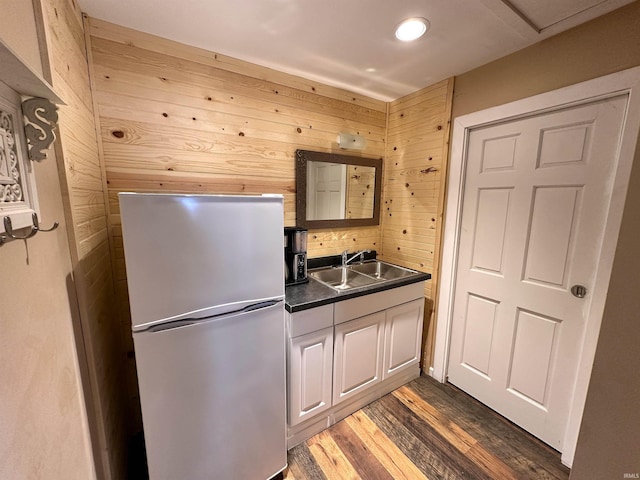 kitchen with freestanding refrigerator, wood walls, dark countertops, a sink, and dark wood finished floors