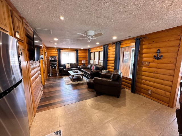 living area with a textured ceiling, rustic walls, a ceiling fan, and light tile patterned floors