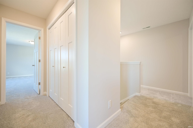 hall with baseboards, visible vents, and light colored carpet