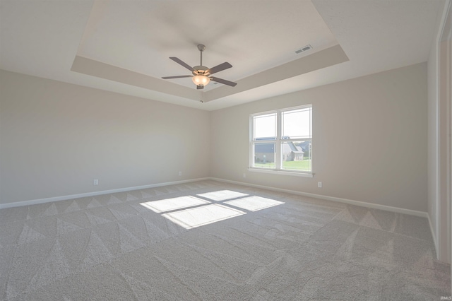 unfurnished room with ceiling fan, visible vents, a raised ceiling, baseboards, and light carpet