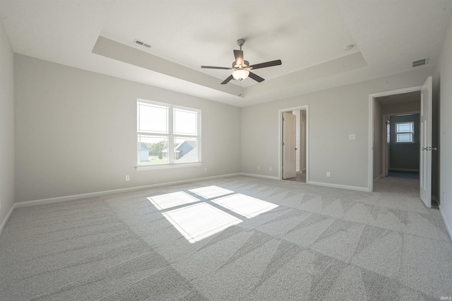unfurnished bedroom with a tray ceiling, visible vents, light carpet, and baseboards