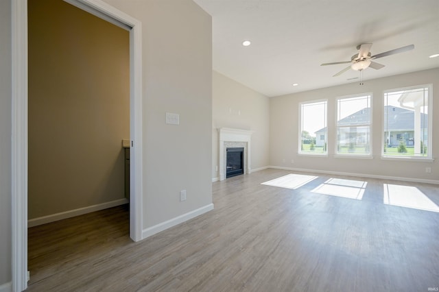 unfurnished living room with a glass covered fireplace, baseboards, ceiling fan, and light wood finished floors