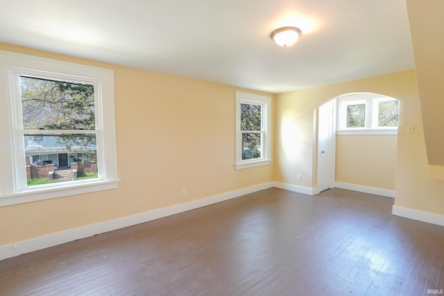 empty room featuring arched walkways, baseboards, and dark wood-type flooring