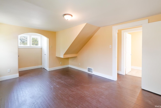 additional living space with arched walkways, baseboards, visible vents, and dark wood-style floors