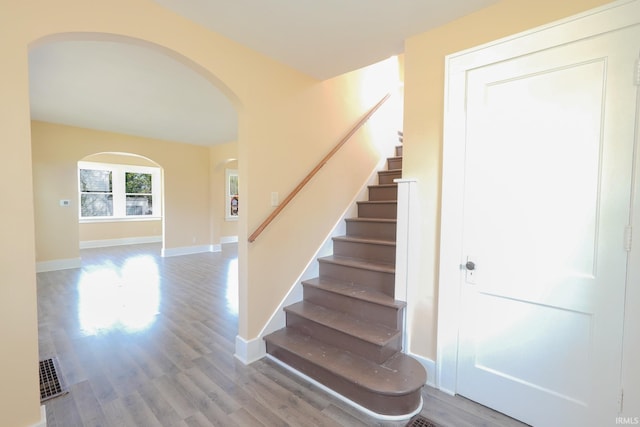 stairs with arched walkways, baseboards, and wood finished floors