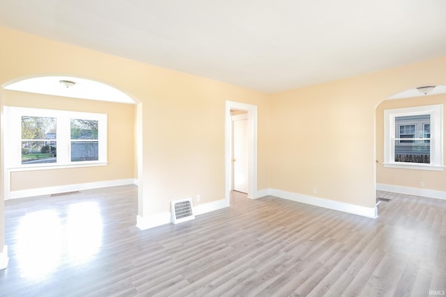 spare room with visible vents, arched walkways, and light wood-type flooring