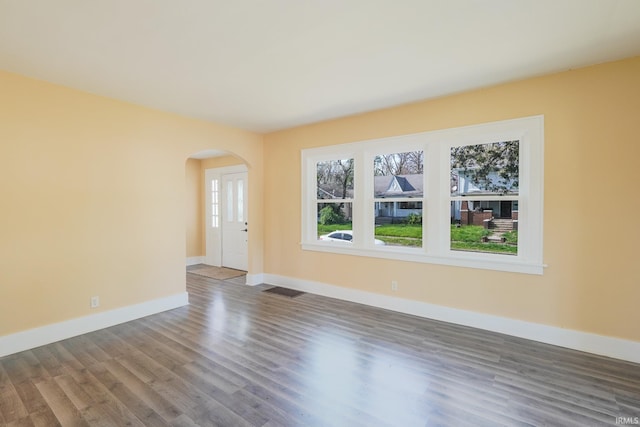 unfurnished room featuring baseboards, arched walkways, wood finished floors, and visible vents