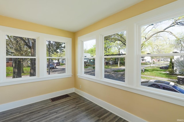 unfurnished sunroom with visible vents, baseboards, wood finished floors, and a healthy amount of sunlight