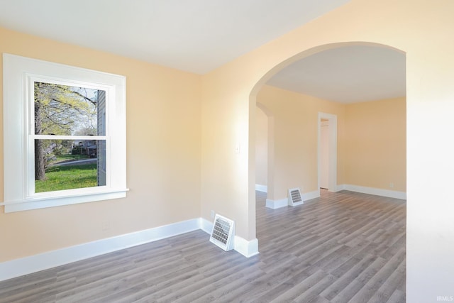 spare room featuring arched walkways, baseboards, wood finished floors, and visible vents