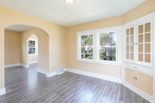 spare room featuring visible vents, arched walkways, plenty of natural light, and wood finished floors