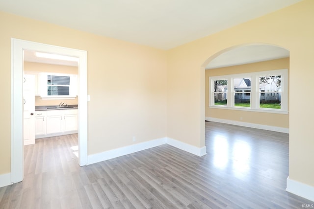 empty room with light wood-type flooring, arched walkways, a sink, and baseboards