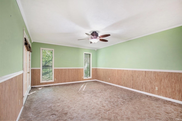 spare room with crown molding, a ceiling fan, wainscoting, and wood walls