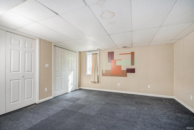 unfurnished bedroom with baseboards, dark colored carpet, and a paneled ceiling