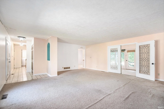 spare room with baseboards, light colored carpet, a textured ceiling, and visible vents