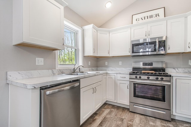 kitchen with light countertops, white cabinets, a sink, appliances with stainless steel finishes, and vaulted ceiling
