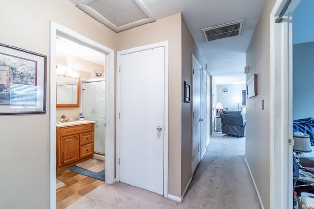 hall featuring visible vents, light carpet, a sink, and attic access