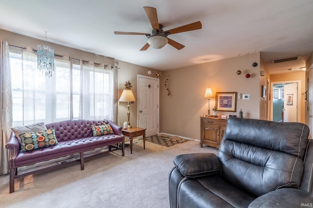 living room featuring visible vents, baseboards, ceiling fan with notable chandelier, and light colored carpet