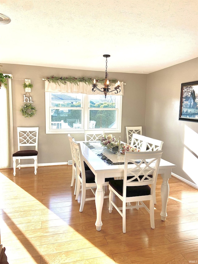 dining space featuring a notable chandelier, a textured ceiling, light wood-style flooring, baseboards, and visible vents