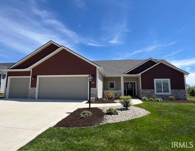 craftsman inspired home featuring an attached garage, a front lawn, driveway, and stone siding