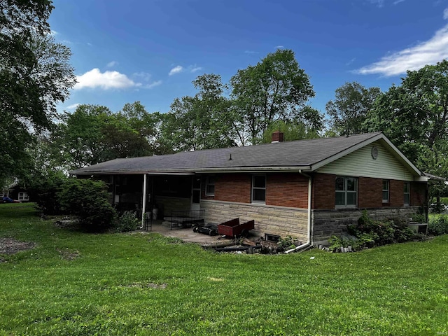 rear view of property with stone siding, a chimney, a shingled roof, a patio area, and a yard