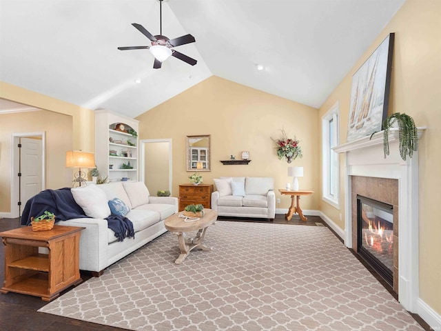 living room with a ceiling fan, baseboards, vaulted ceiling, and a glass covered fireplace