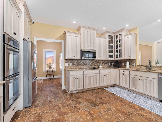 kitchen featuring decorative backsplash, appliances with stainless steel finishes, a sink, baseboards, and stone tile flooring