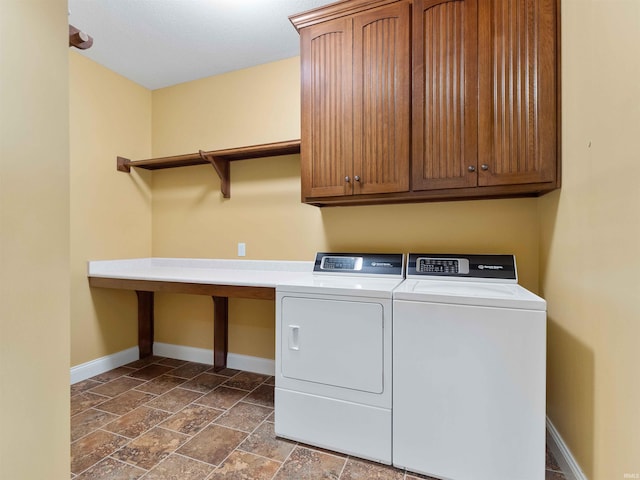 laundry room featuring baseboards, cabinet space, washer and dryer, and stone tile flooring
