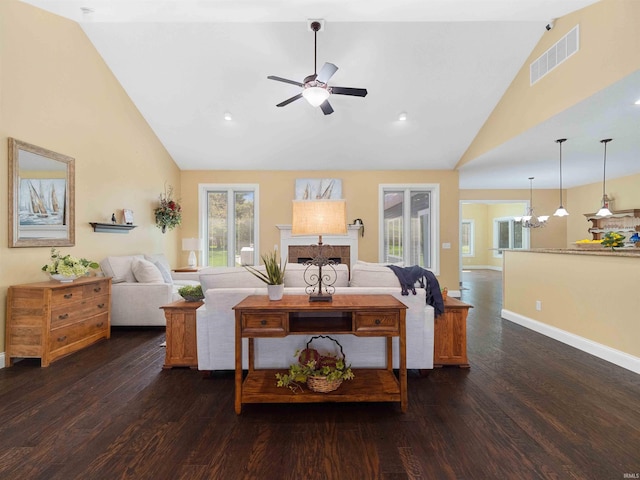 living room with high vaulted ceiling, ceiling fan with notable chandelier, a tile fireplace, and visible vents