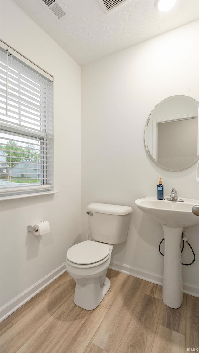 half bathroom with baseboards, toilet, and wood finished floors