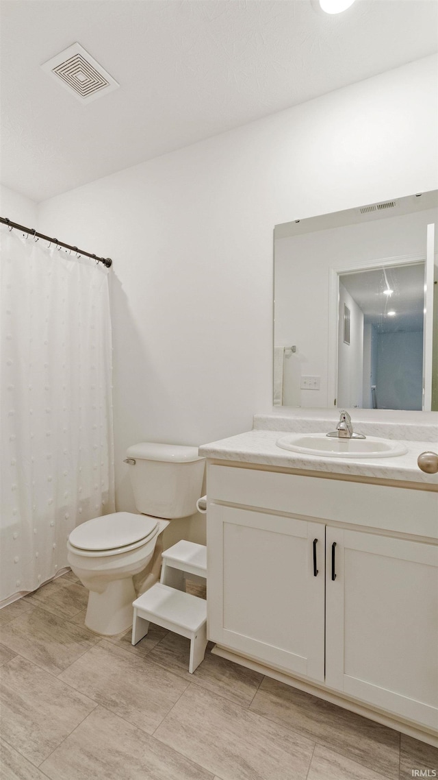 full bathroom with vanity, a shower with shower curtain, toilet, and visible vents