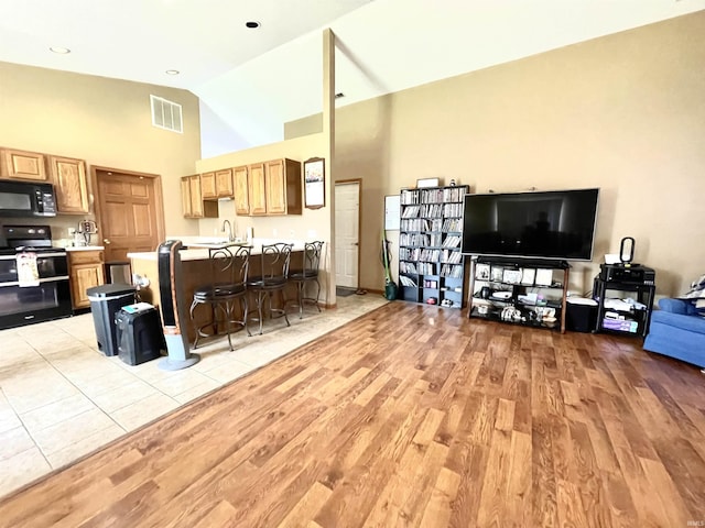 living room with high vaulted ceiling, light wood-type flooring, and visible vents