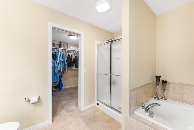 bathroom featuring baseboards, a walk in closet, a garden tub, and a stall shower