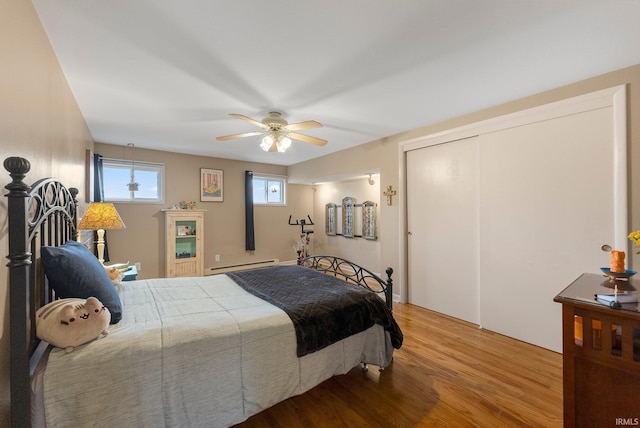 bedroom with light wood-style floors, a baseboard radiator, a ceiling fan, and a closet