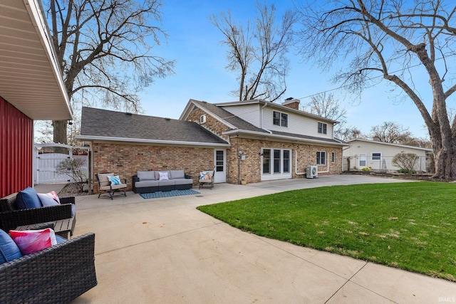rear view of property with a patio, roof with shingles, an outdoor living space, brick siding, and a lawn