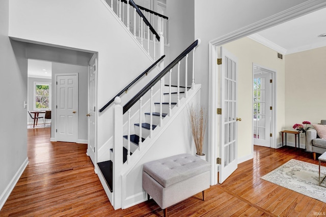 staircase with crown molding, baseboards, visible vents, and wood finished floors