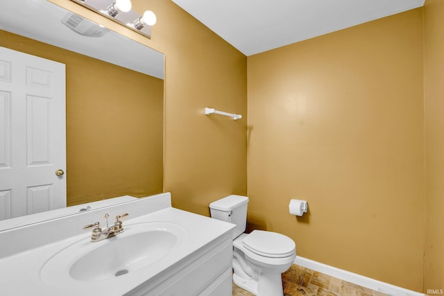 bathroom with vanity, toilet, stone finish floor, baseboards, and visible vents