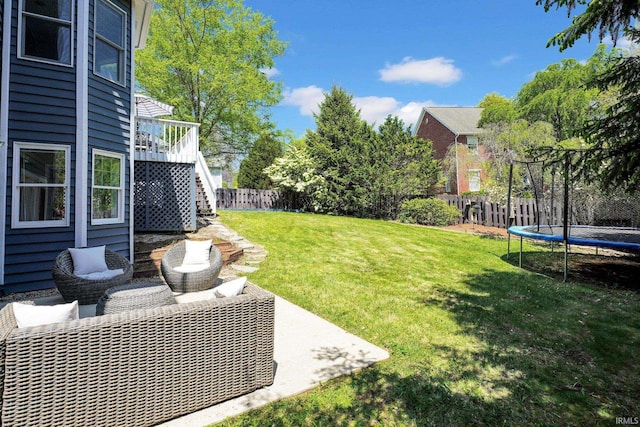 view of yard with a trampoline, stairs, a wooden deck, a fenced backyard, and a patio