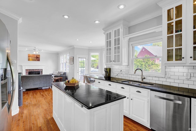 kitchen featuring dark countertops, a sink, a brick fireplace, stainless steel appliances, and ornamental molding
