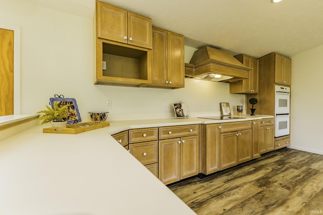 kitchen with black electric stovetop, light countertops, white double oven, premium range hood, and dark wood-type flooring
