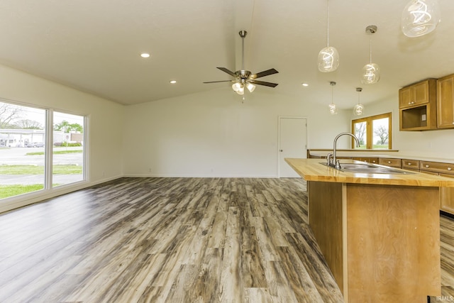 kitchen with lofted ceiling, wood finished floors, wooden counters, a center island with sink, and a sink
